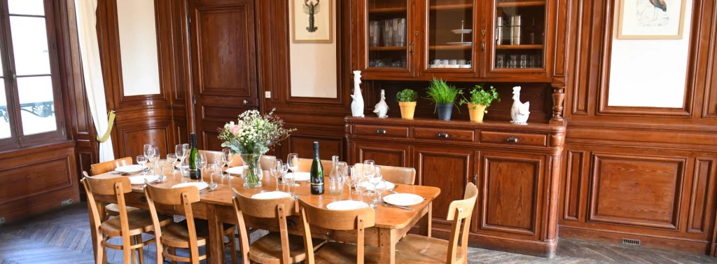Table dressée avec assiettes, couverts, verres, bouteilles de vin et décorations florales, pour un dîner de cérémonie organisé dans un gîte de mariage en Normandie, dans la salle de réception du domaine.